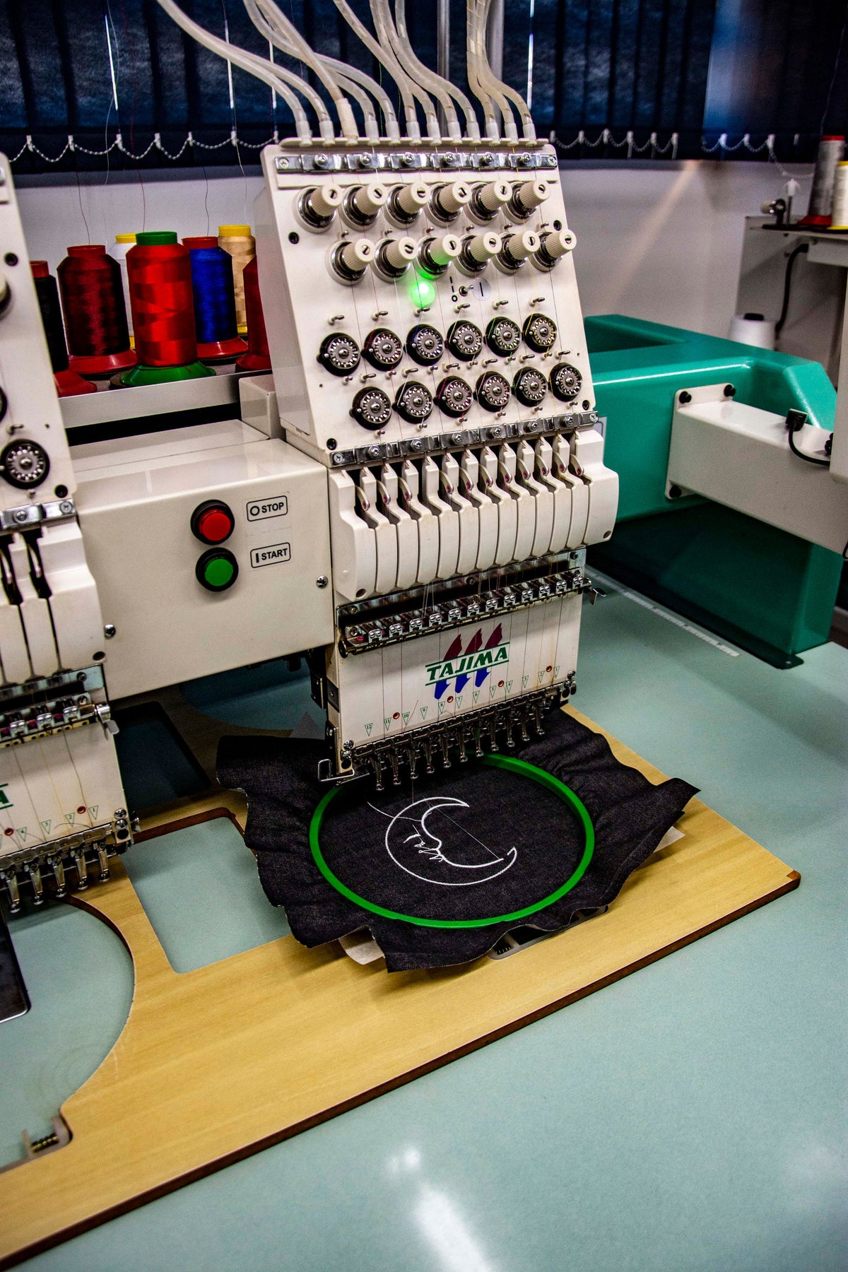 Industrial embroidery machine stitching a design on dark twill held in a hoop
