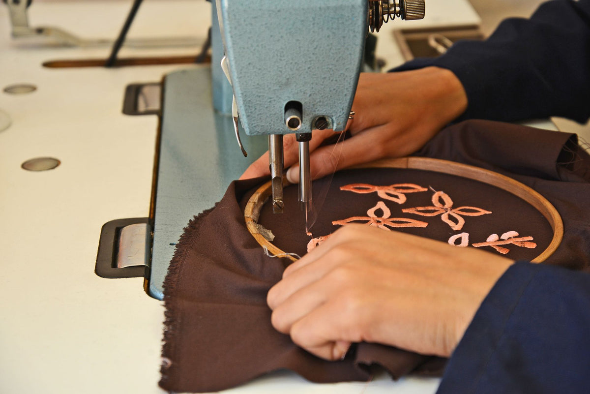 Hands guiding a hooped fabric under an embroidery machine needle